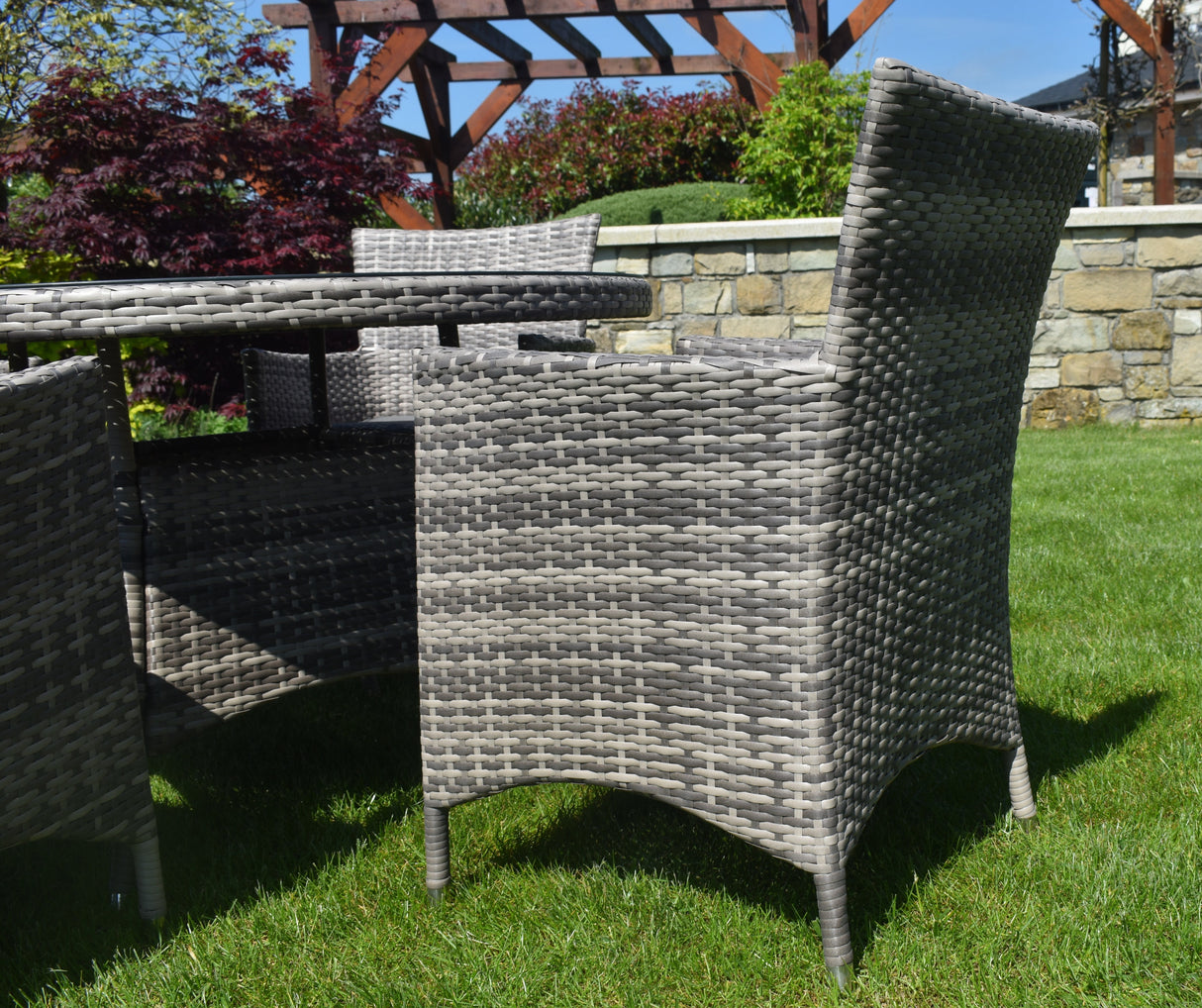 Gray wicker chair and table set in a garden with a stone wall and trees in the background furniture store ni