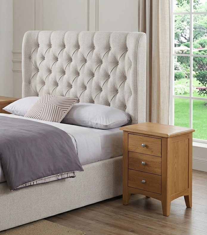 Kilkenny large solid oak 3-drawer nightstand, showing off its natural wood grain, curved top, and sleek chrome handles in a modern bedroom at the furniture store ni