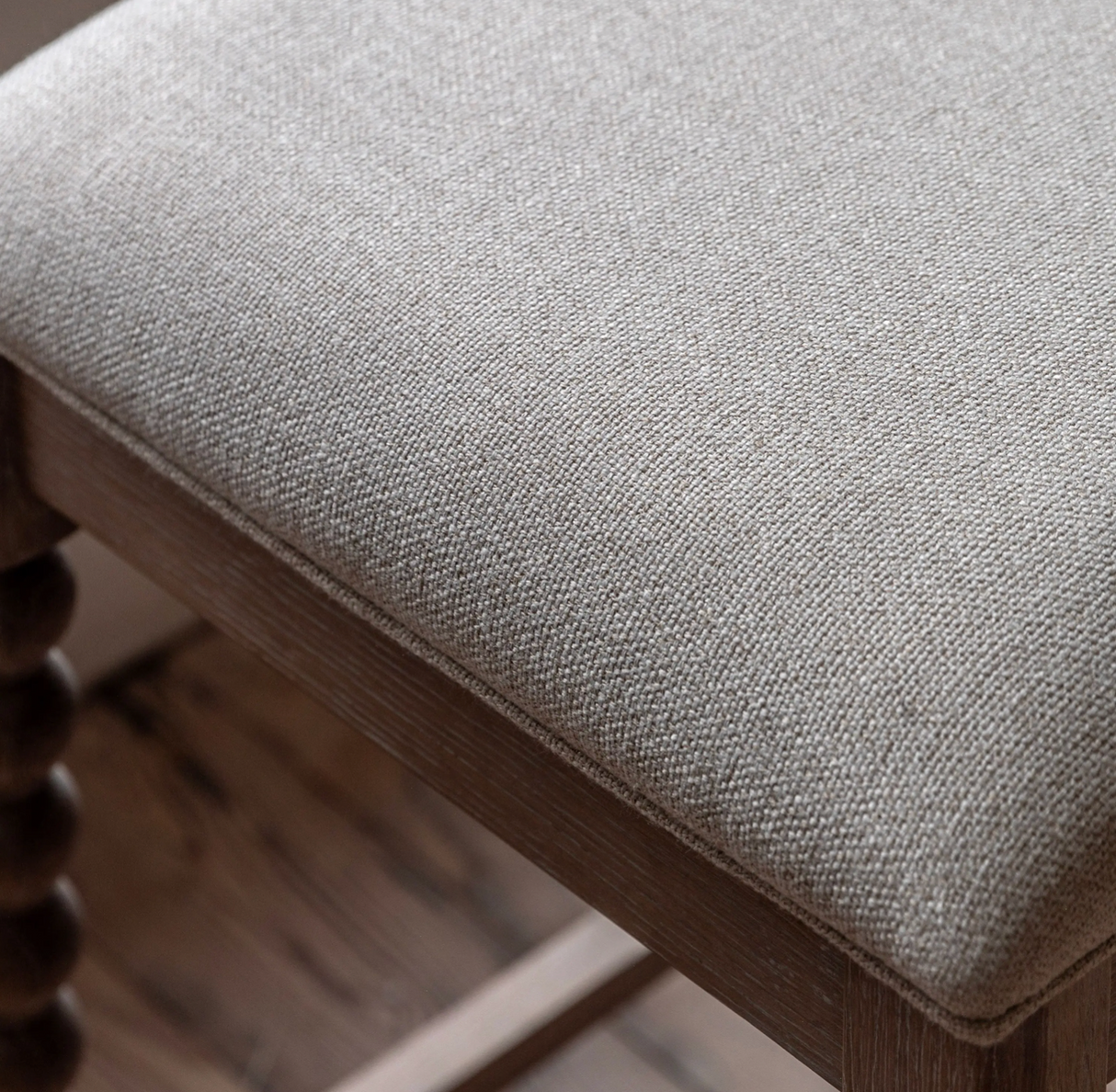 Artisan oak bar stool showcasing its exquisite hand-crafted bobbin turned legs, premium lime wash finish, and a luxurious biscuit-coloured upholstered seat at the furniture store ni