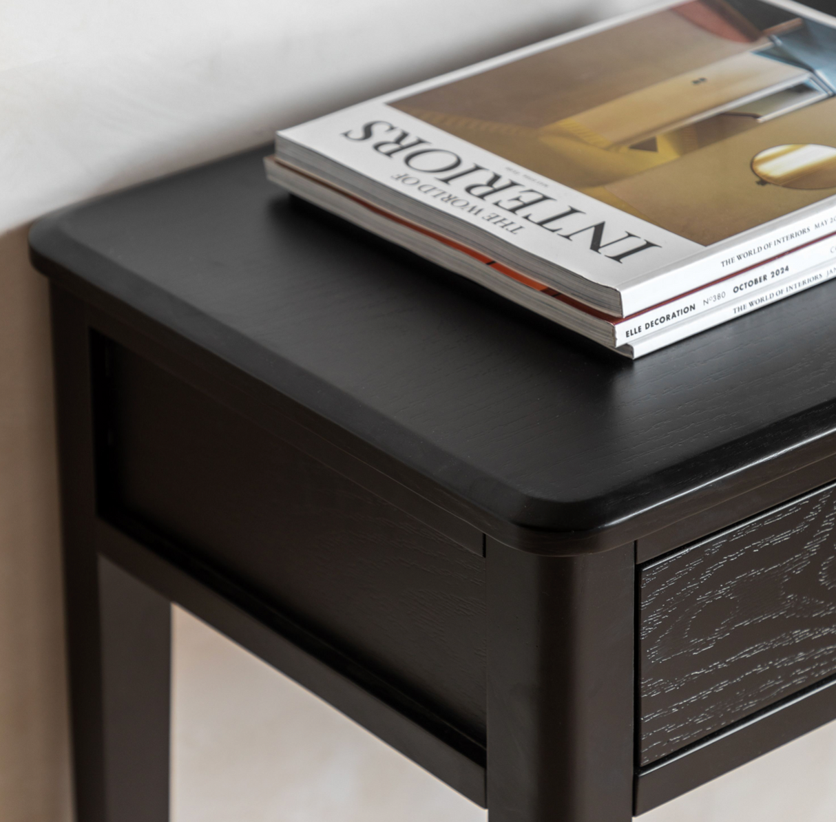 Black nightstand with a stack of magazines on top