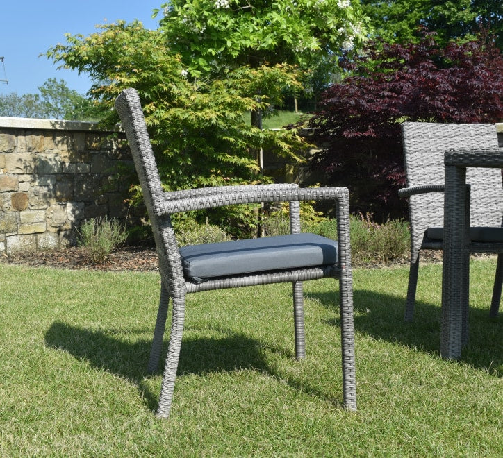Outdoor chair with cushion on grass, stone wall, and trees in background at the furniture store ni