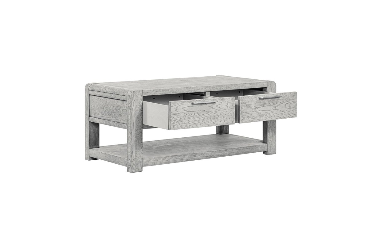 A modern low-profile coffee table in a light gray wood grain finish, featuring three drawers on the front with one open, and an open lower shelf.
