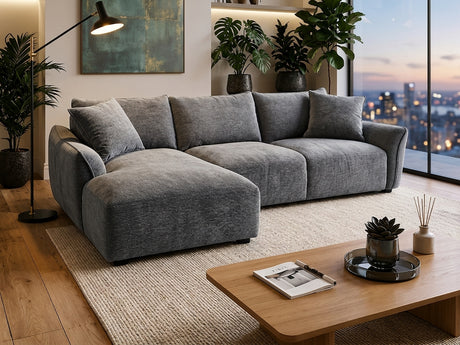the bowman is a modern gray fabric sectional sofa with a chaise lounge, styled in a contemporary living room with a wooden coffee table, potted plants, and a large window overlooking a city skyline at dusk available at the furniture store ni
