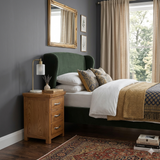 Cozy bedroom with green wingback bed, wooden nightstand, and large window.