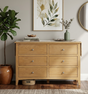 Kilkenny 6-drawer wide solid oak chest, showcasing its rich natural wood grain, curved top profile, and sleek chrome handles in a contemporary bedroom layout at the furniture store ni.