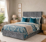 Bedroom with Prime grey upholstered bed, blue and white floral bedding, and wooden nightstands at furniture store ni