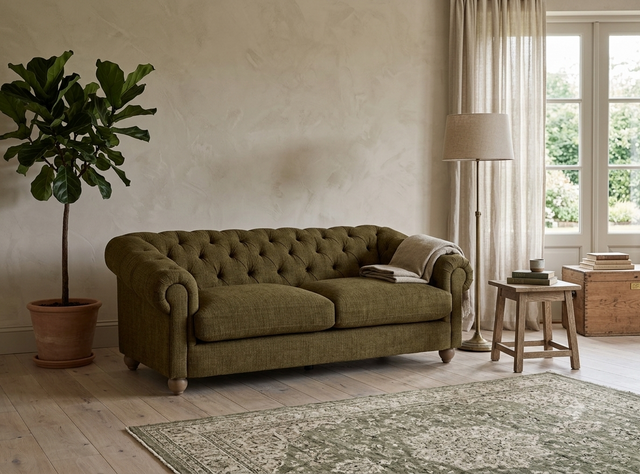 Modern 3-seater Chesterfield sofa showcasing its deep-buttoned back, elegant scrolled arms, and gracefully contoured silhouette sitting on solid ash legs at the furniture store ni