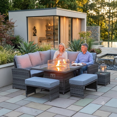 Outdoor amalfi patio conversation set with a dark woven wicker sectional sofa, two matching ottomans, a side table, and a glass-top fire pit table with visible flames, shown with a couple sitting and a modern pool house in the background at furniture store ni 