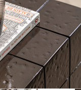 close up of Novara contemporary side table crafted from charcoal brown glazed glass concrete, showcasing its compact block profile and retro faux tile surface pattern at the furniture store ni