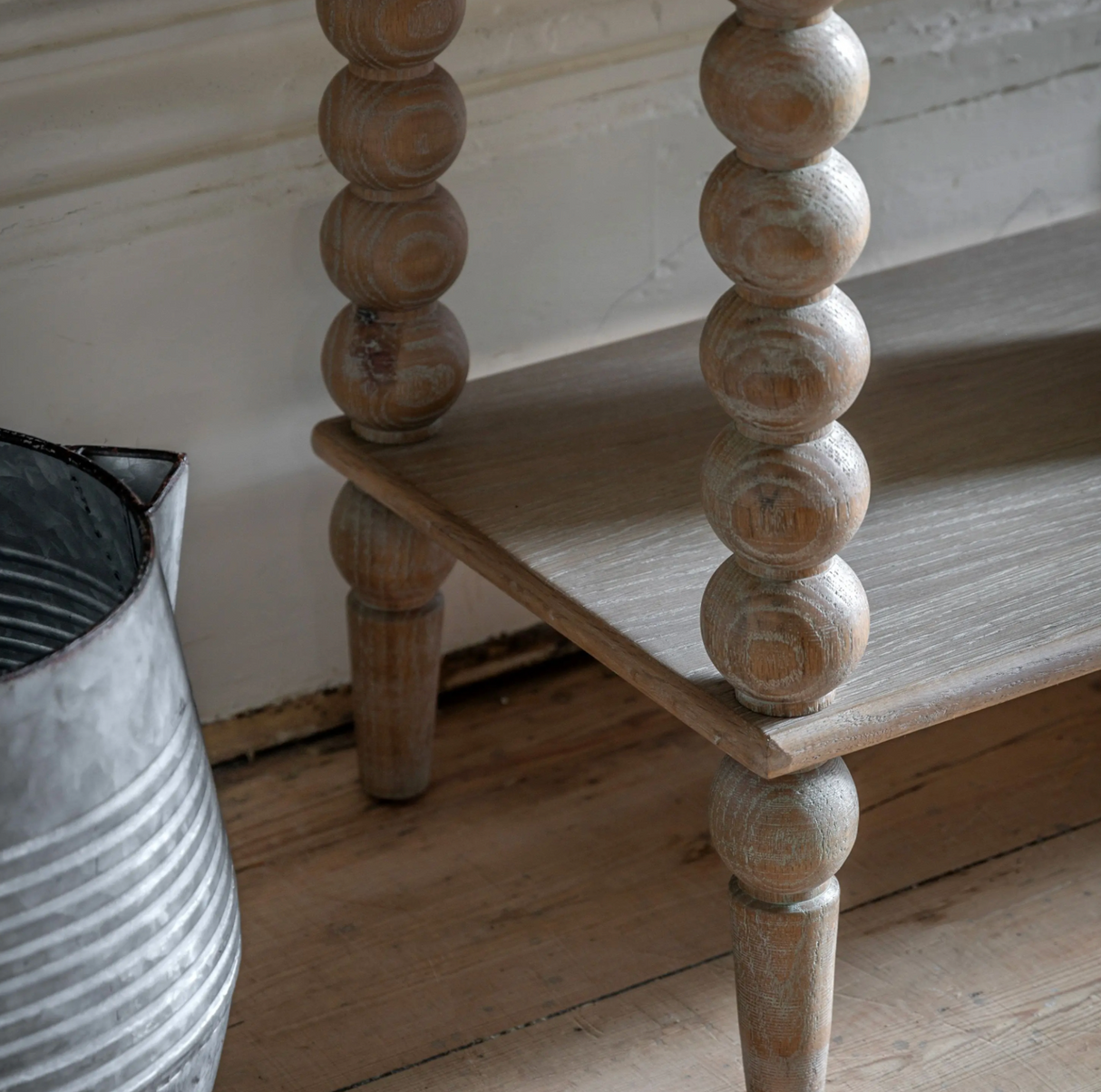 Wooden shelf with spool legs next to a metal bin on a wooden floor.