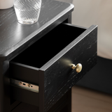 Black drawer with a gold handle on a wooden surface.