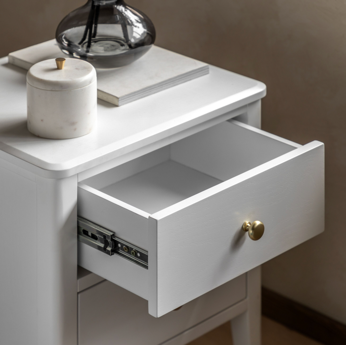 White nightstand with open drawer, decorative items on top, and a brown background.