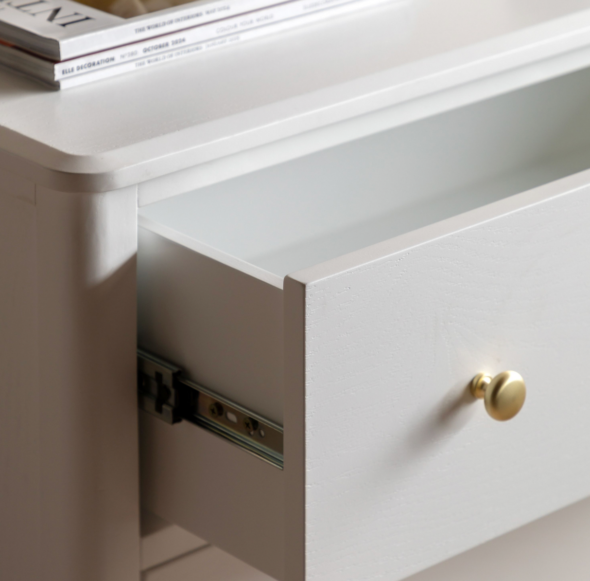 Close-up of a white drawer with a gold handle and visible hardware.