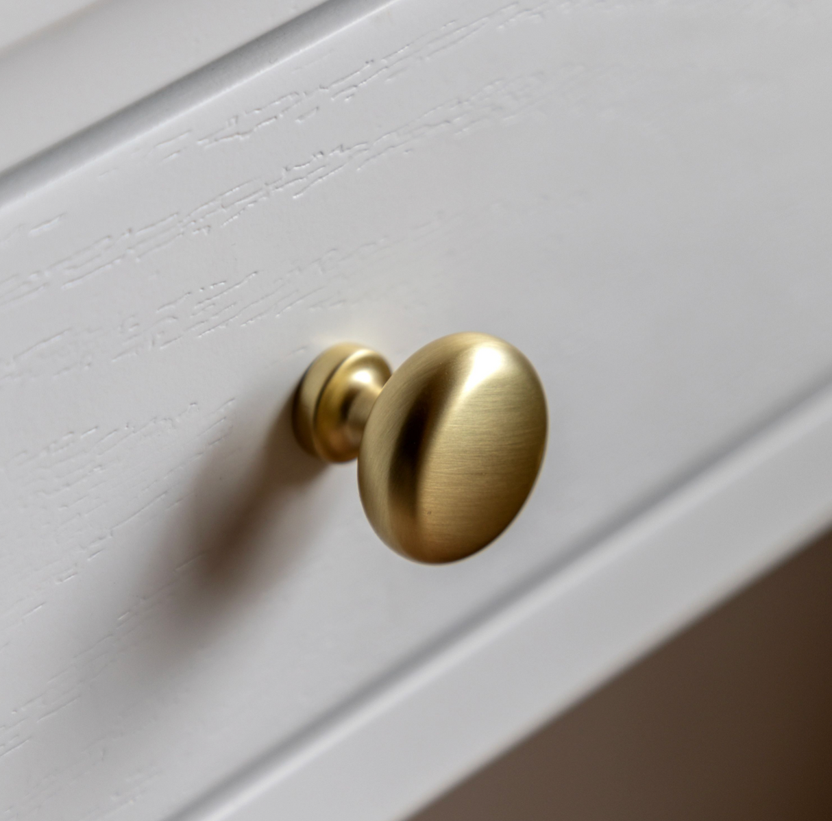 Gold cabinet knob on a white wooden surface