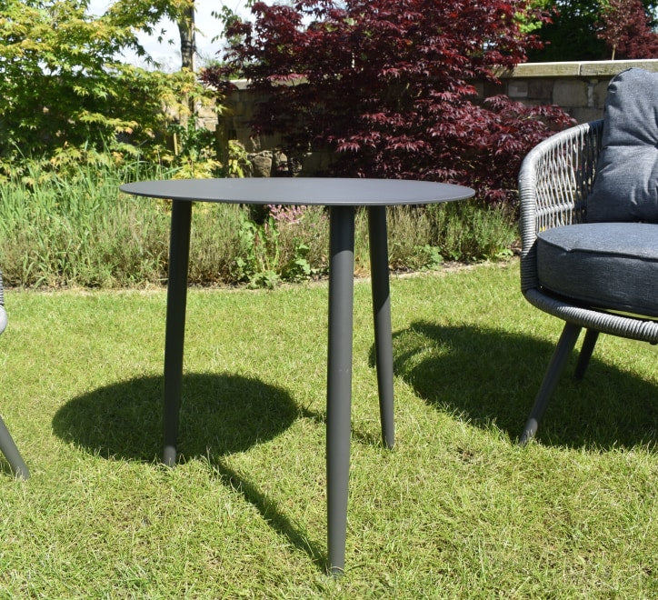 Gray outdoor table in a garden setting with a chair and greenery furniture store ni