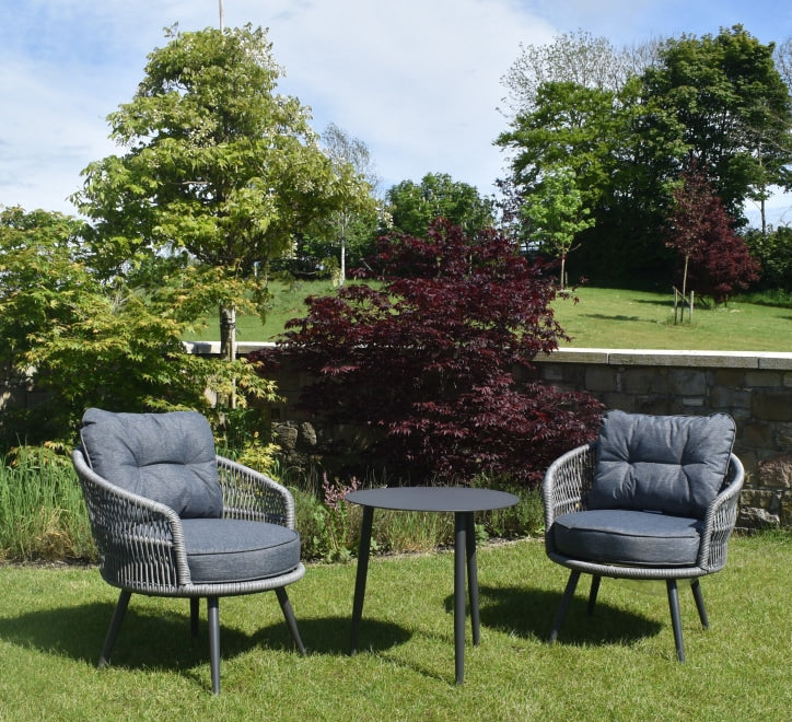 Venice garden bistro set featuring two rattan armchairs with plush grey cushions and a black side table on a patio at the furniture store ni
